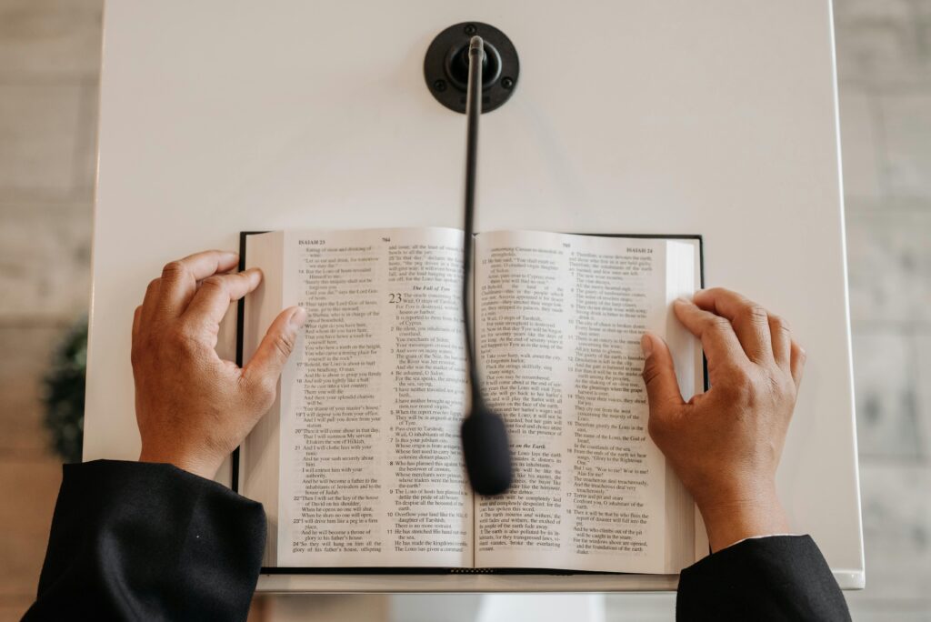Hands holding an open Bible on a podium with a microphone. Ideal for religious or public speaking themes.