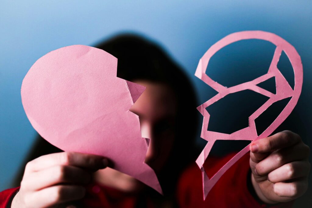 Close-up of hands holding a pink broken paper heart, symbolizing love and heartbreak. Separar