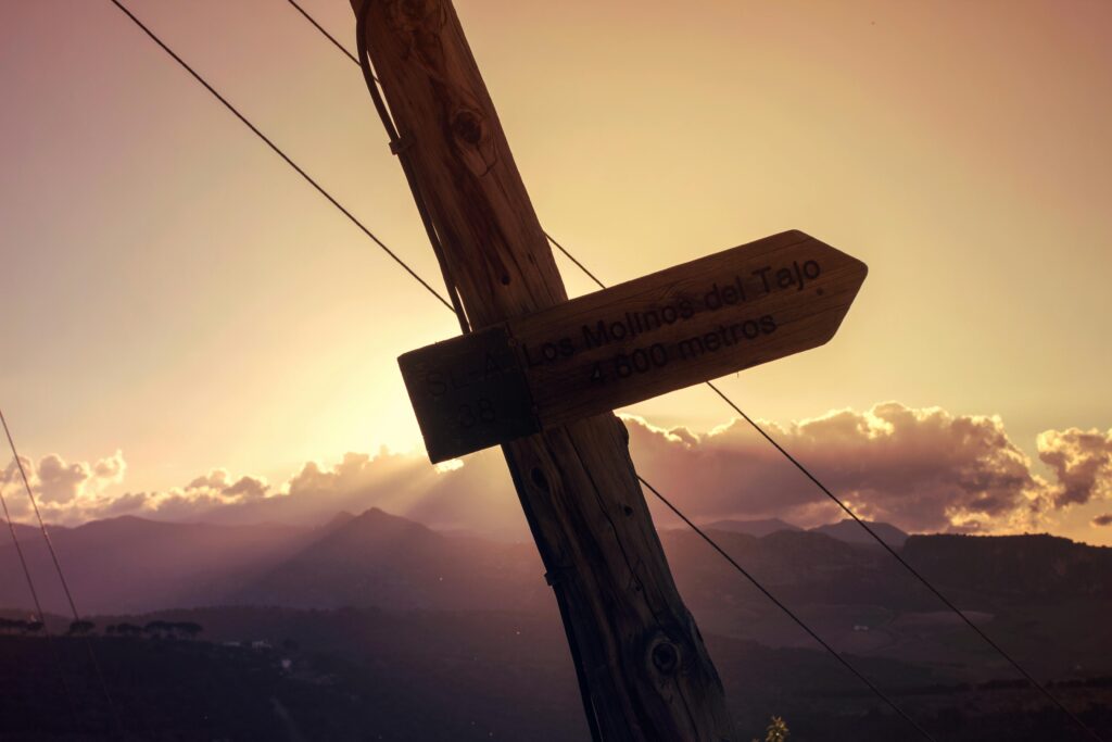 Scenic sunset view with a wooden signpost in Ronda, Spain, guiding to Los Molinos del Tajo. Predestinación