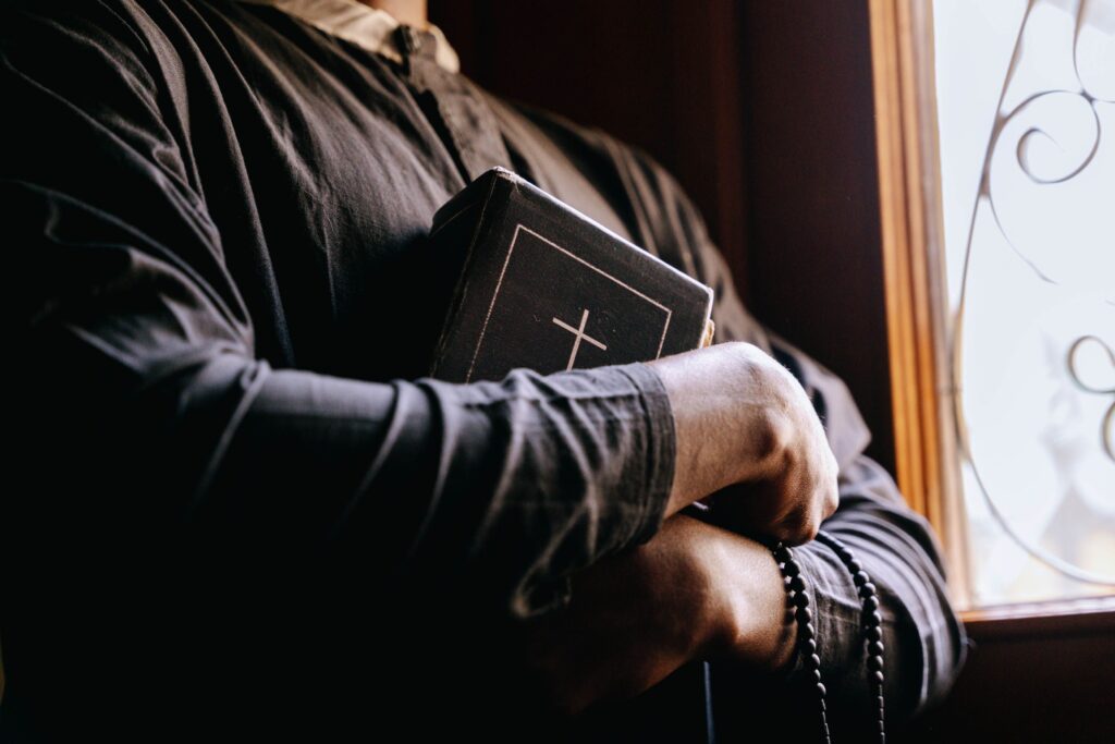 A priest holding a Bible by a sunlit window, symbolizing faith and spirituality. Cristianismo