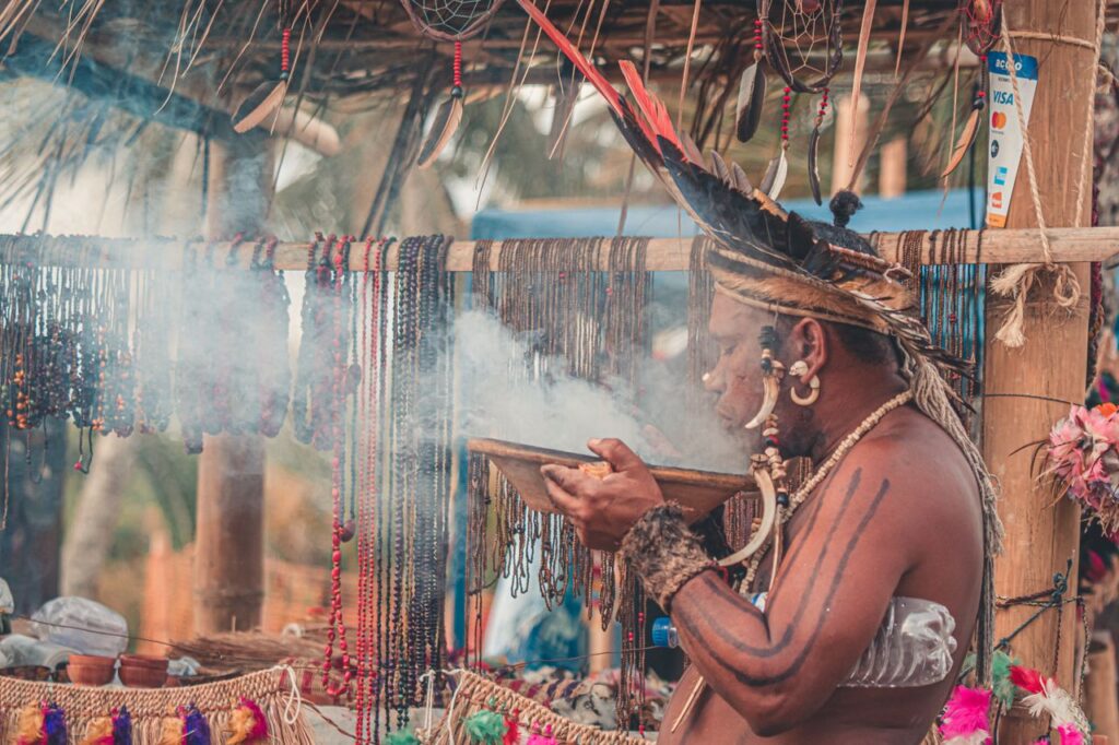 A man in traditional attire participates in an African ceremony, surrounded by smoke and ornaments.