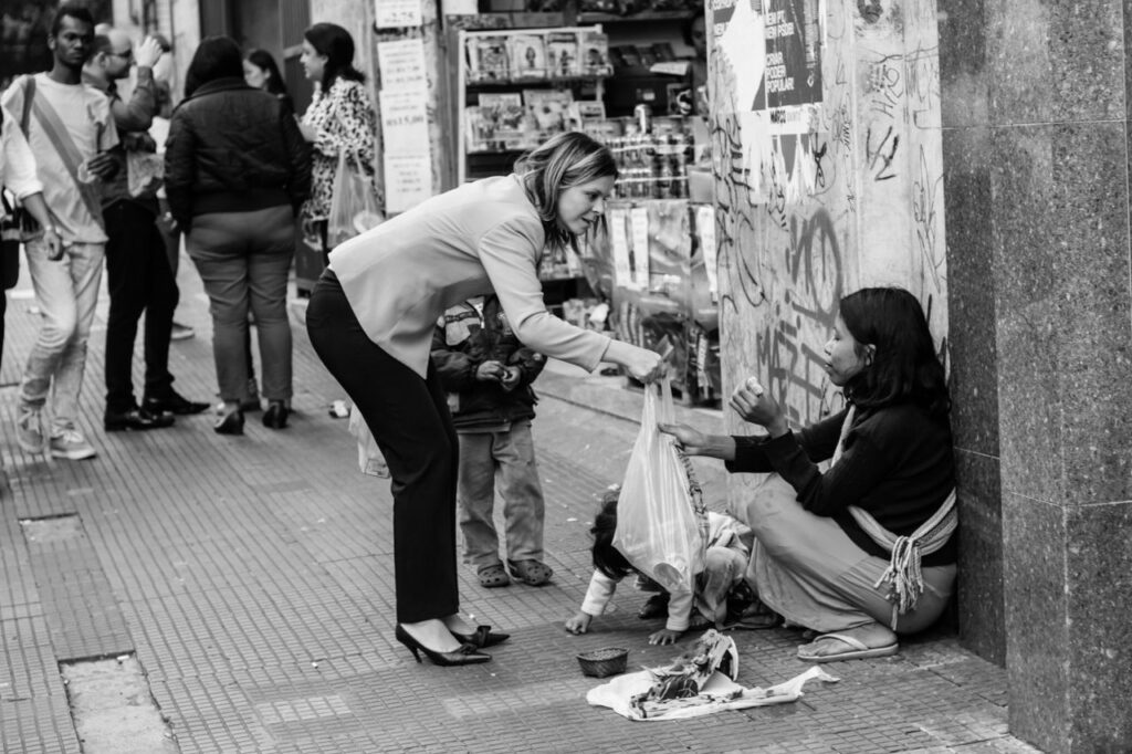 A street interaction in São Paulo showing a woman giving a bag to a mother and child. Acuerdo