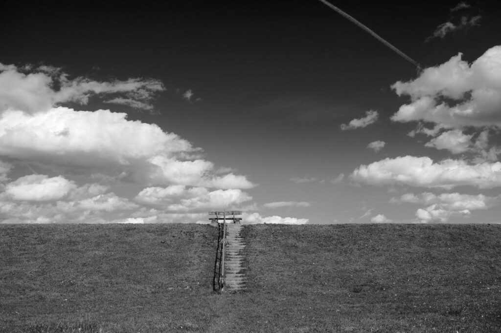 A minimalist black and white landscape featuring a stairway leading to the sky. Acuerdo