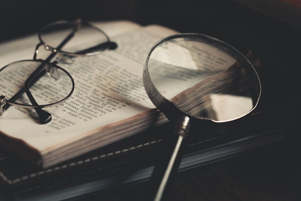 Detailed close-up of an open book with a magnifying glass and eyeglasses, emphasizing discovery and exploration. Marta